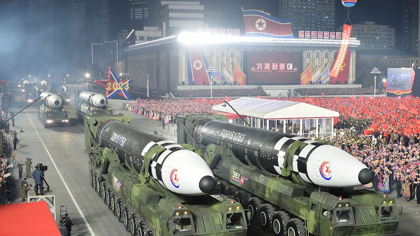 Two missiles on display with a crowd in the background. 