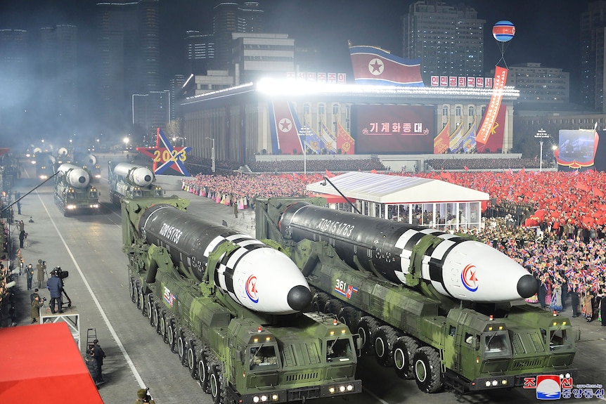 Two missiles on display with a crowd in the background. 
