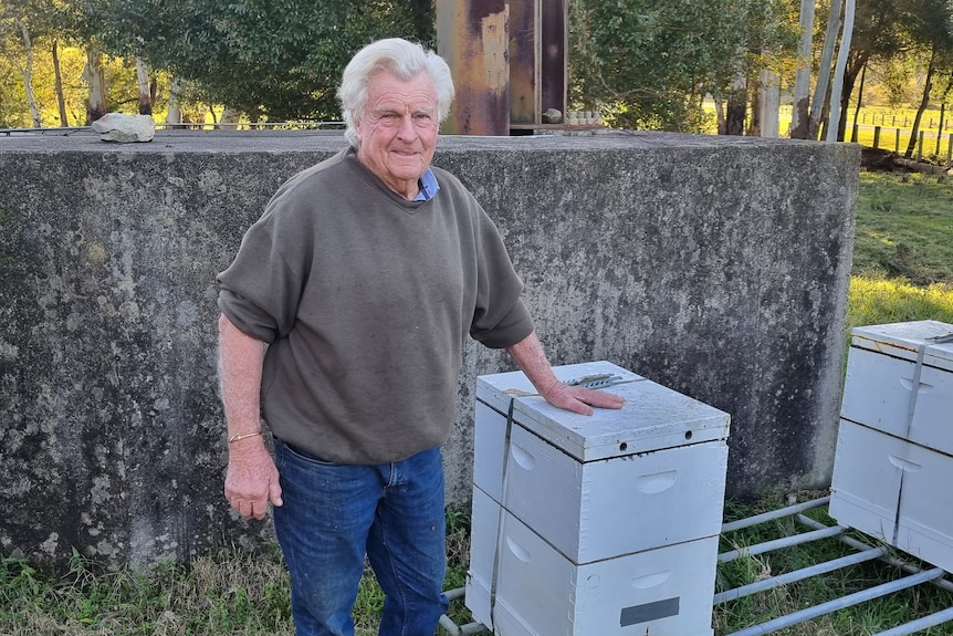 Elderly man standing next to a beehive.