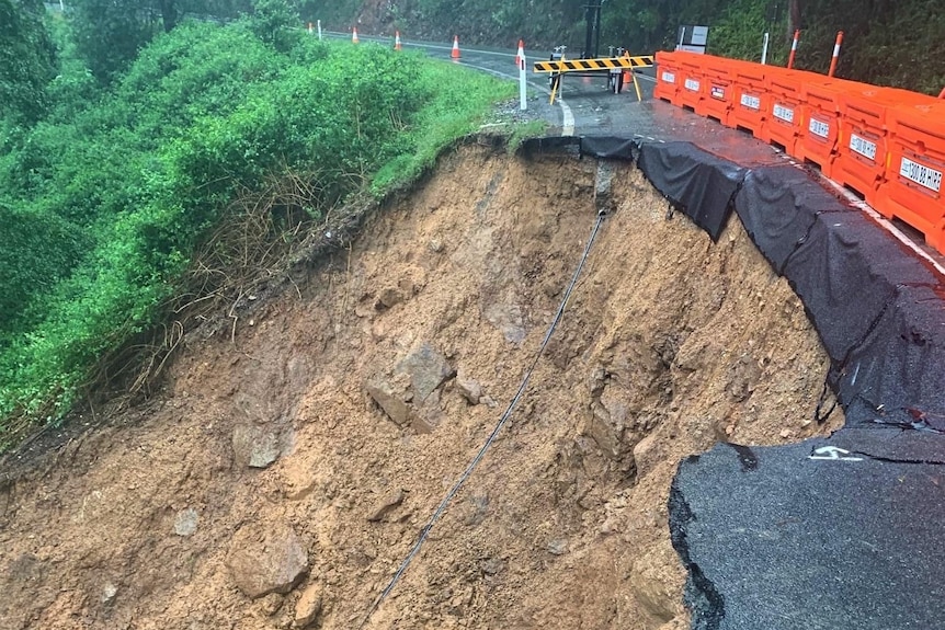 A road is half eroded, showing soil and rock where the road should run. 