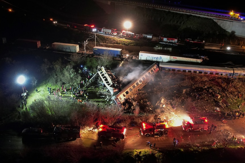An aerial view shows smoking derailed train carriages illuminated by the colourful headlights of emergency vehicles.