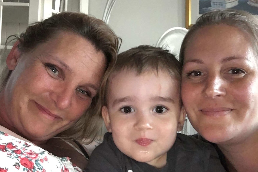 Two women and a toddler smile for a selfie.