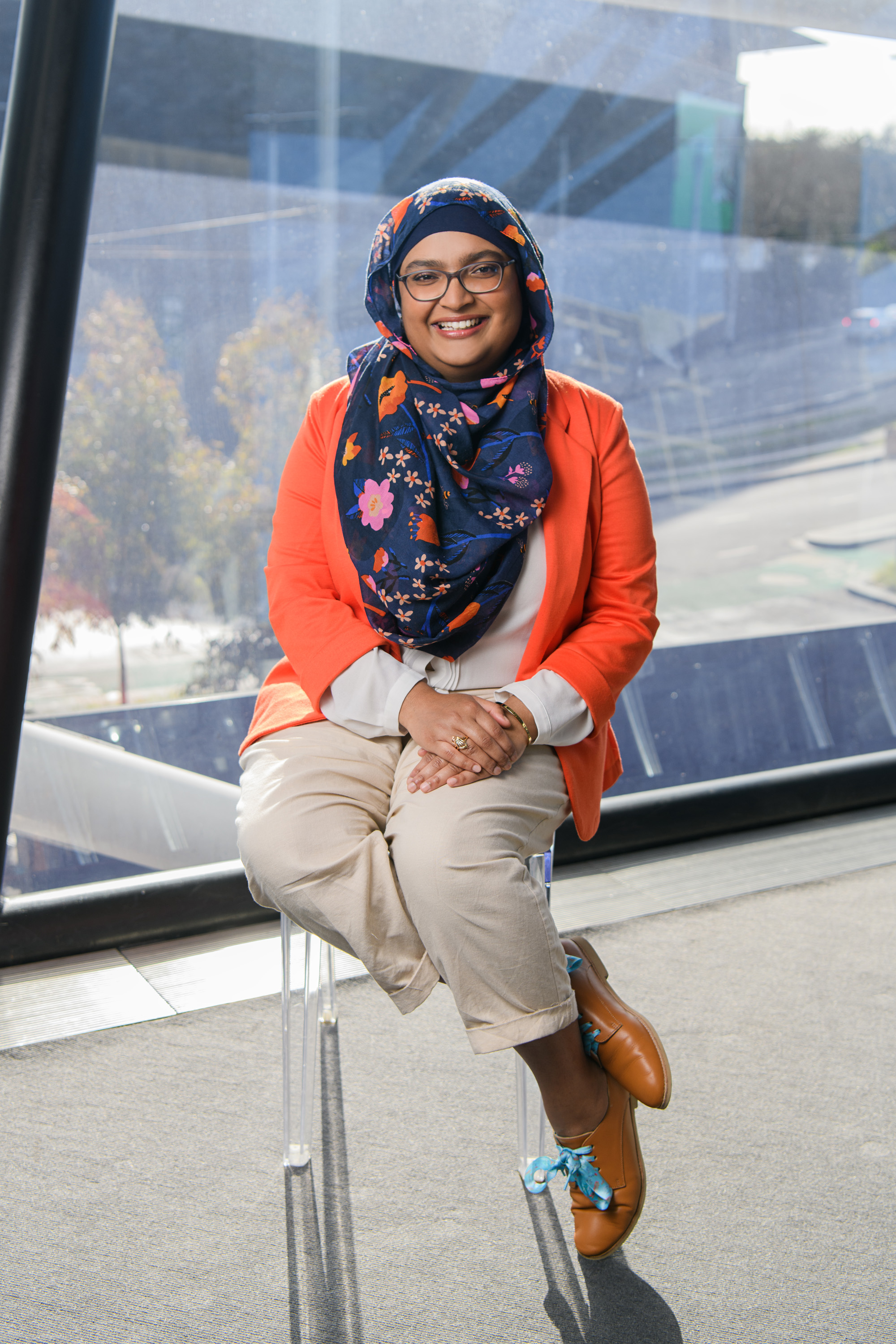A Muslim Australian woman wearing a headscarf smiles widely into the camera. She is seated in a theatre foyer.