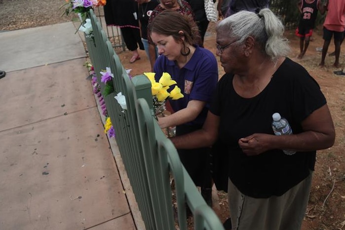 Two women put flowers on a fence as part of the vigil.