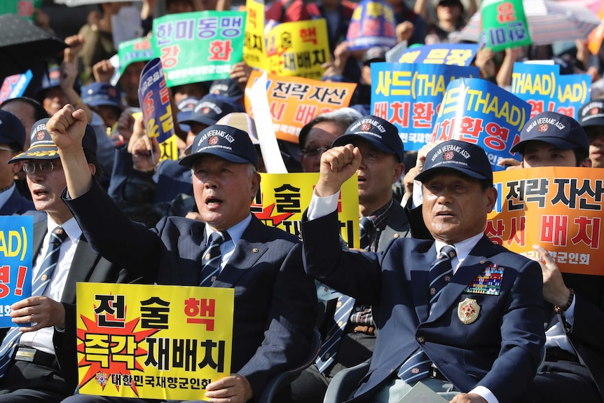 Men in uniform chant with their hands in the air as they hold protest signs in Korean language.