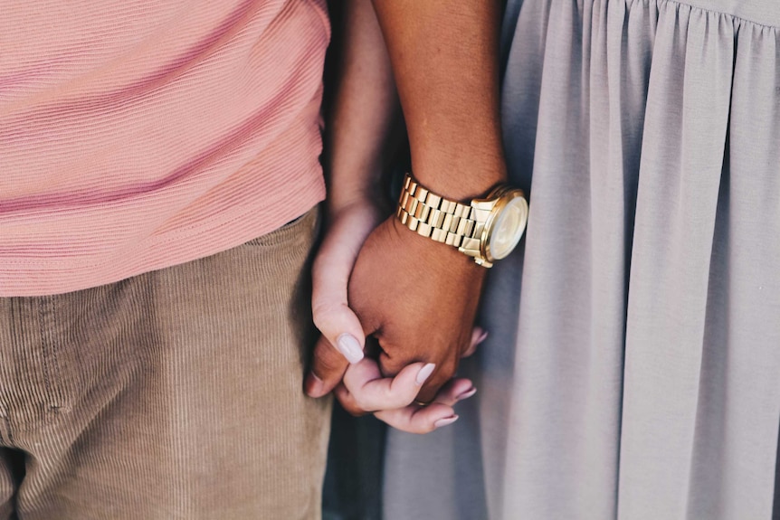 A man and woman stand close and hold hands to depict the support a partner can offer in times of financial or debt stress.
