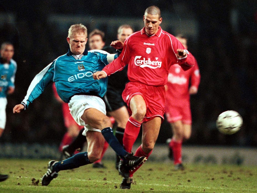 A football defender grimaces as he gets his foot across an opposition player to kick the ball away during a match.