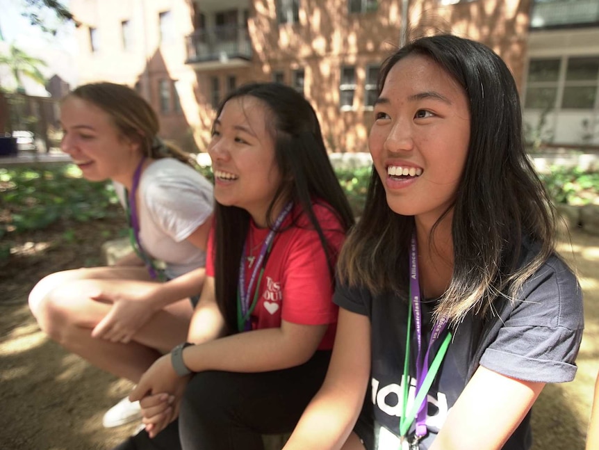 Lier Deng (r) a teenage girl sits with friends outside a brick building at the Girls’  Student Leadership Conference in Sydney.