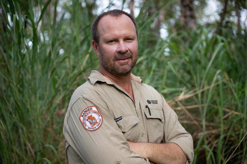 a man with a NT Parks uniform looking at the camera with gamba grass behind him.
