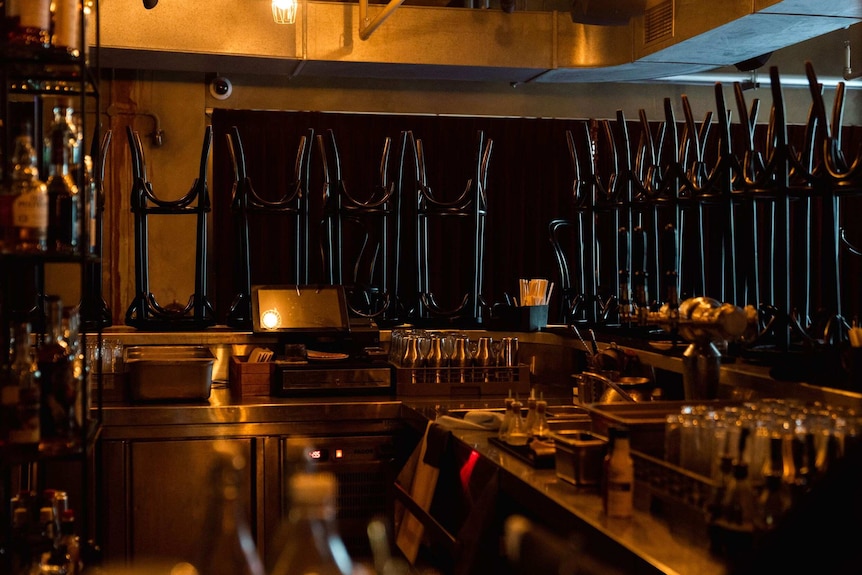 An empty bar with stools lined up on top of the bench and glass racks full.