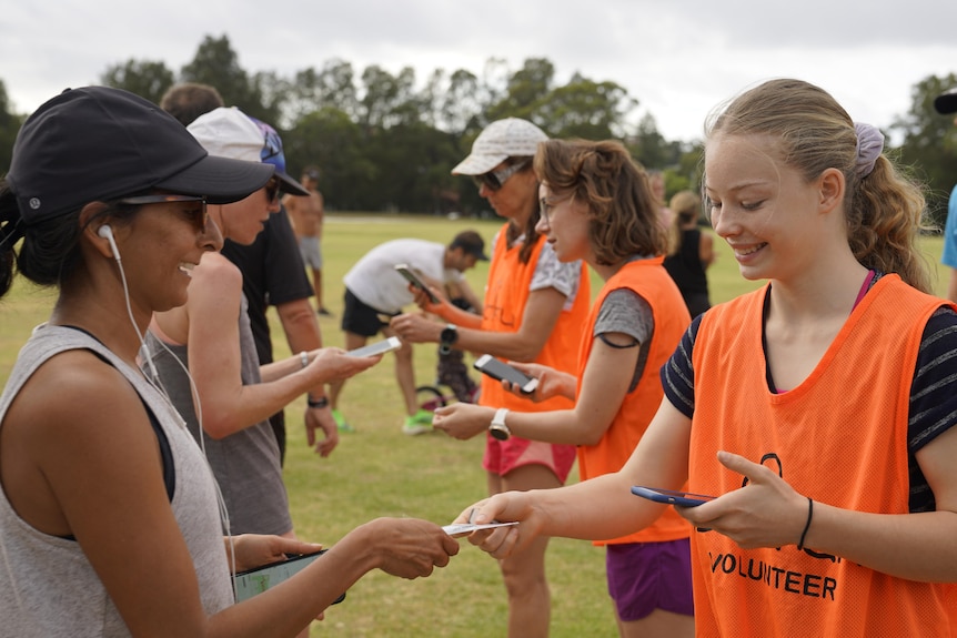 A woman hands a token to another woman after parkrun.