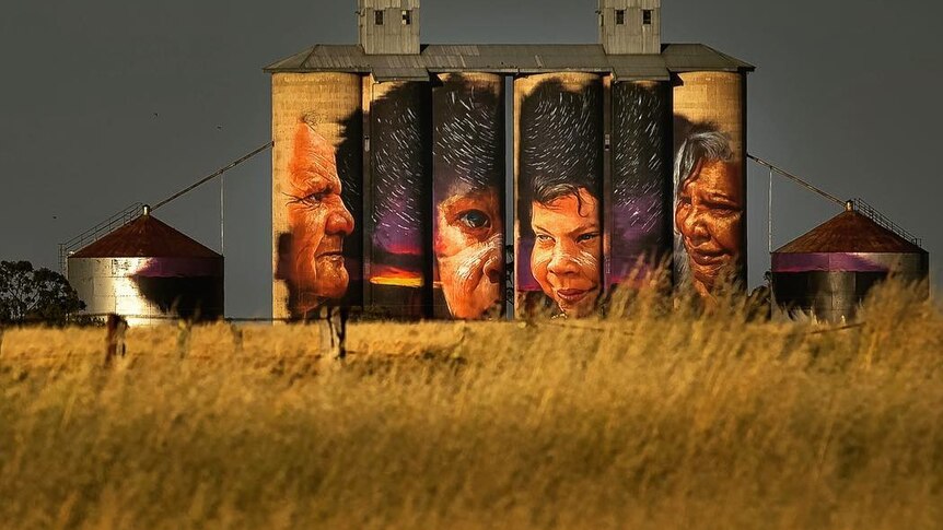 Silo covered in a painting of faces and a night sky.