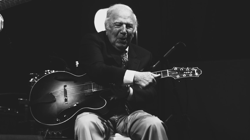 A monochrome shot of guitarist Bucky Pizzarelli on-stage playing his seven-string guitar