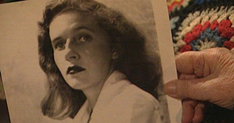A wrinkled hand holds a black and white photo of a young woman seemingly from the 1950s.