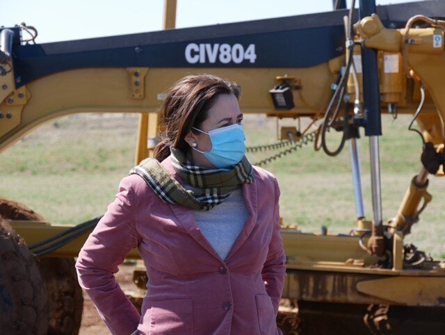 Annastacia Palaszczuk stands with her hands behind her back in front of earthmoving equipment.