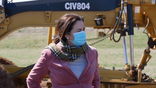 Annastacia Palaszczuk stands with her hands behind her back in front of earthmoving equipment.
