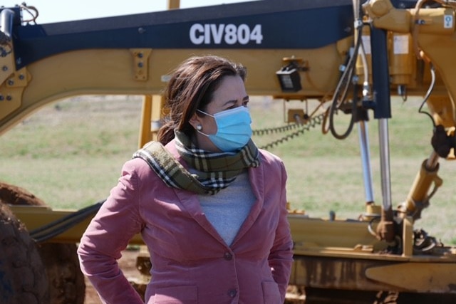 Annastacia Palaszczuk stands with her hands behind her back in front of earthmoving equipment.