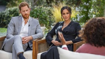 Harry and Meghan sit in chairs facing Oprah Winfrey who has her back to the camera.