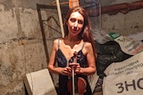 Woman in  a basement smiling to the camera while holding a violin