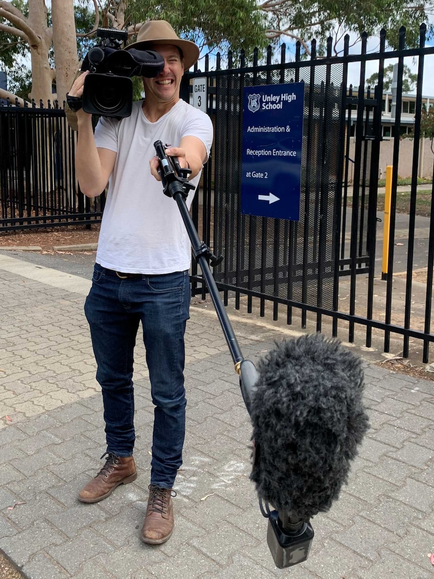 Rothall with camera on shoulder and boom mic on pole in other hand.