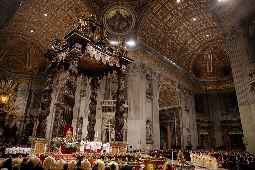 A wide angle photo shows the ornate ceilings of St Peter's Basilica as the floor is filled with dignitaries and cardinals.