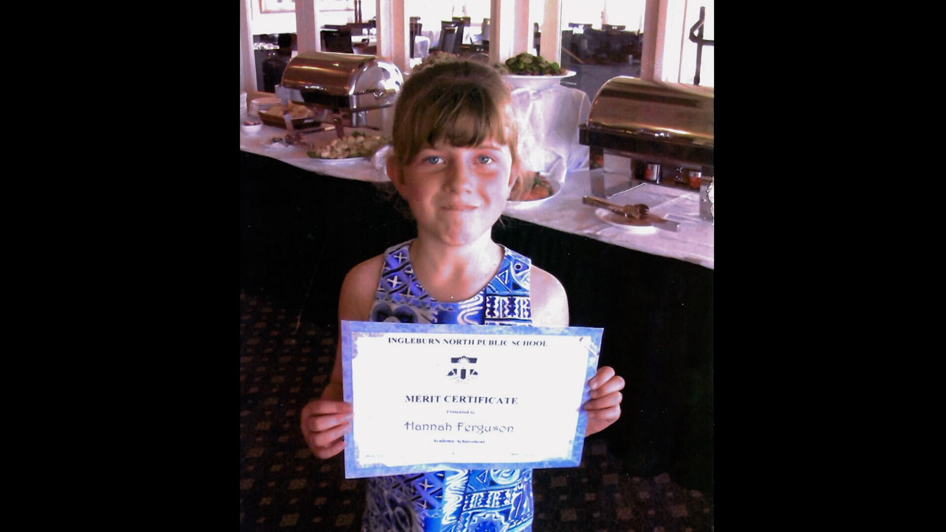 A female primary school student proudly holds up her school achievement award.