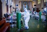 A man in full PPE moves a giant oxygen tank through a church filled with hospital beds 