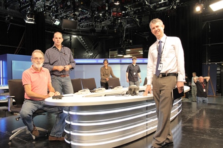 Eric Napper standing next to desk in studio surrounded by production crew.
