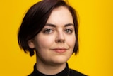 Portrait of a young woman, art historian Alice Procter, looking at the camera, yellow backdrop