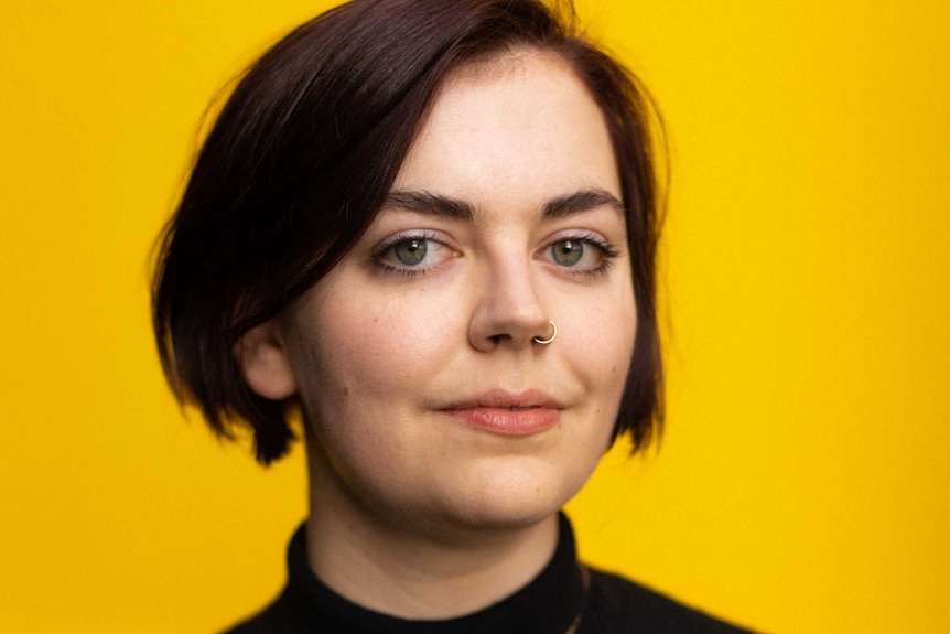 Portrait of a young woman, art historian Alice Procter, looking at the camera, yellow backdrop