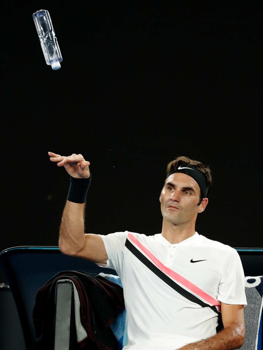 A seated Federer tosses a water bottle in the air.