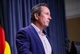 Mark McGowan standing at a lectern with a serious expression.