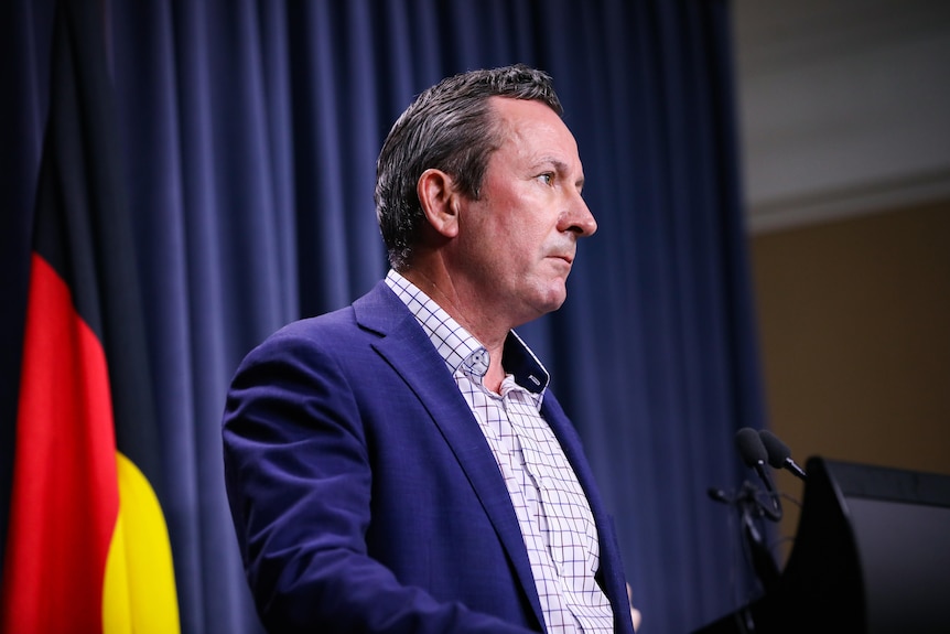Mark McGowan standing at a lectern with a serious expression.