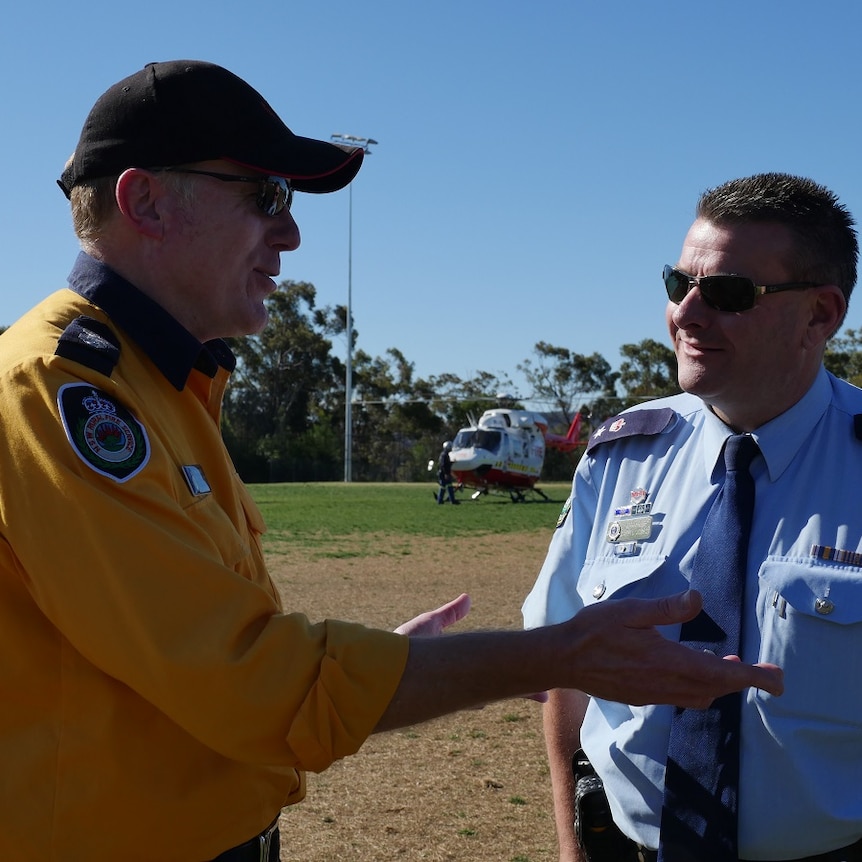 Member of New South Wales Rural Fire Service and member of the New South Wales Police force in discussion in front of helicopter