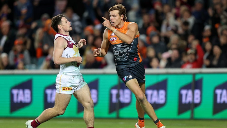 A GWS forward points his finger in celebration as a Brisbane defender reacts.