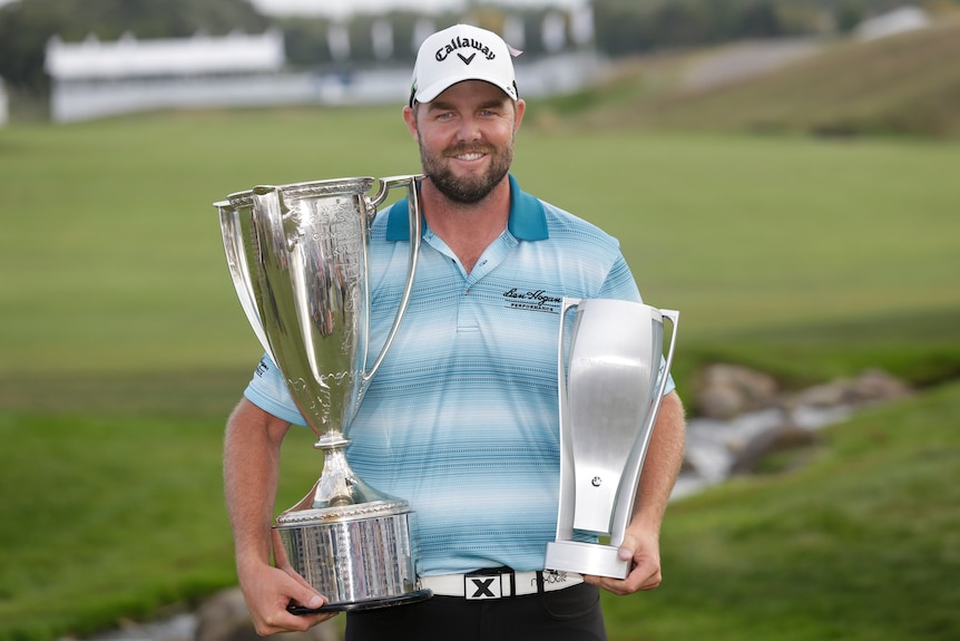 Marc Leishman smiles as he poses with the Wadley Cup, left, and the BMW Championship trophy.