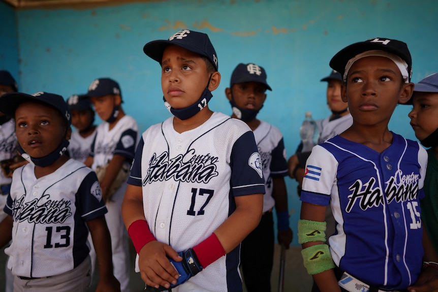 Niños del equipo de béisbol de Centro Habana escuchan instrucciones de un entrenador de béisbol durante un partido en La Habana