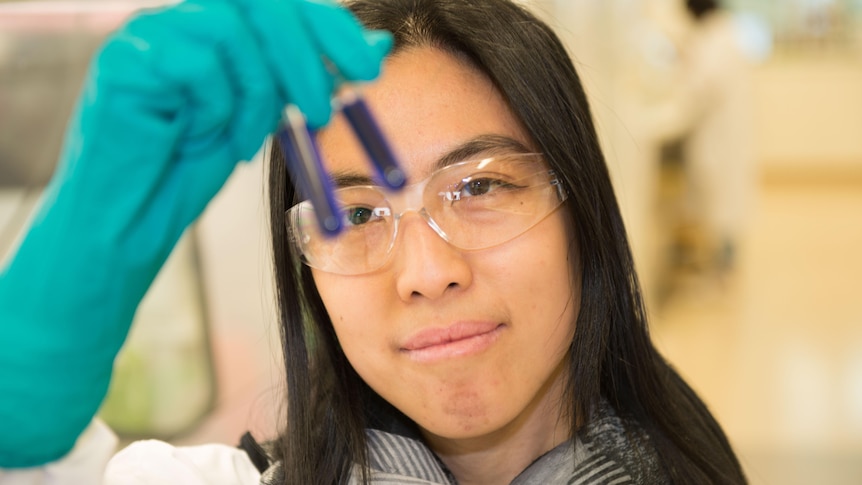 Dr Amy Chung is wearing lab kit and looking at vials. He has a serious expression.