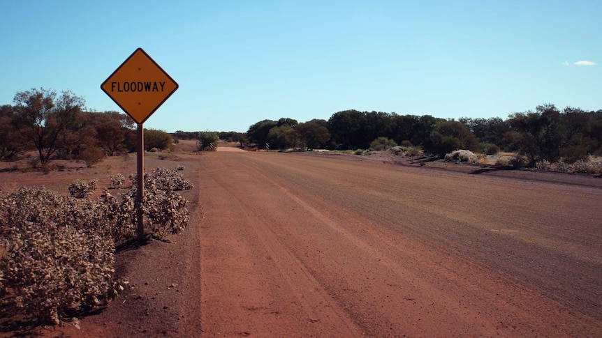 Red dirt road with sign warning of floodway