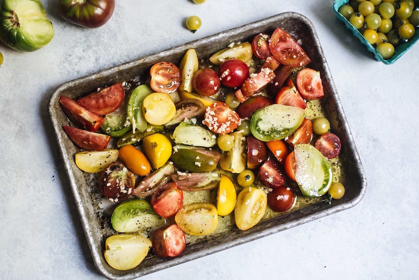 Heirloom and cherry tomatoes in a baking tray with sea salt, ready to be roasted for a caprese salad recipe.