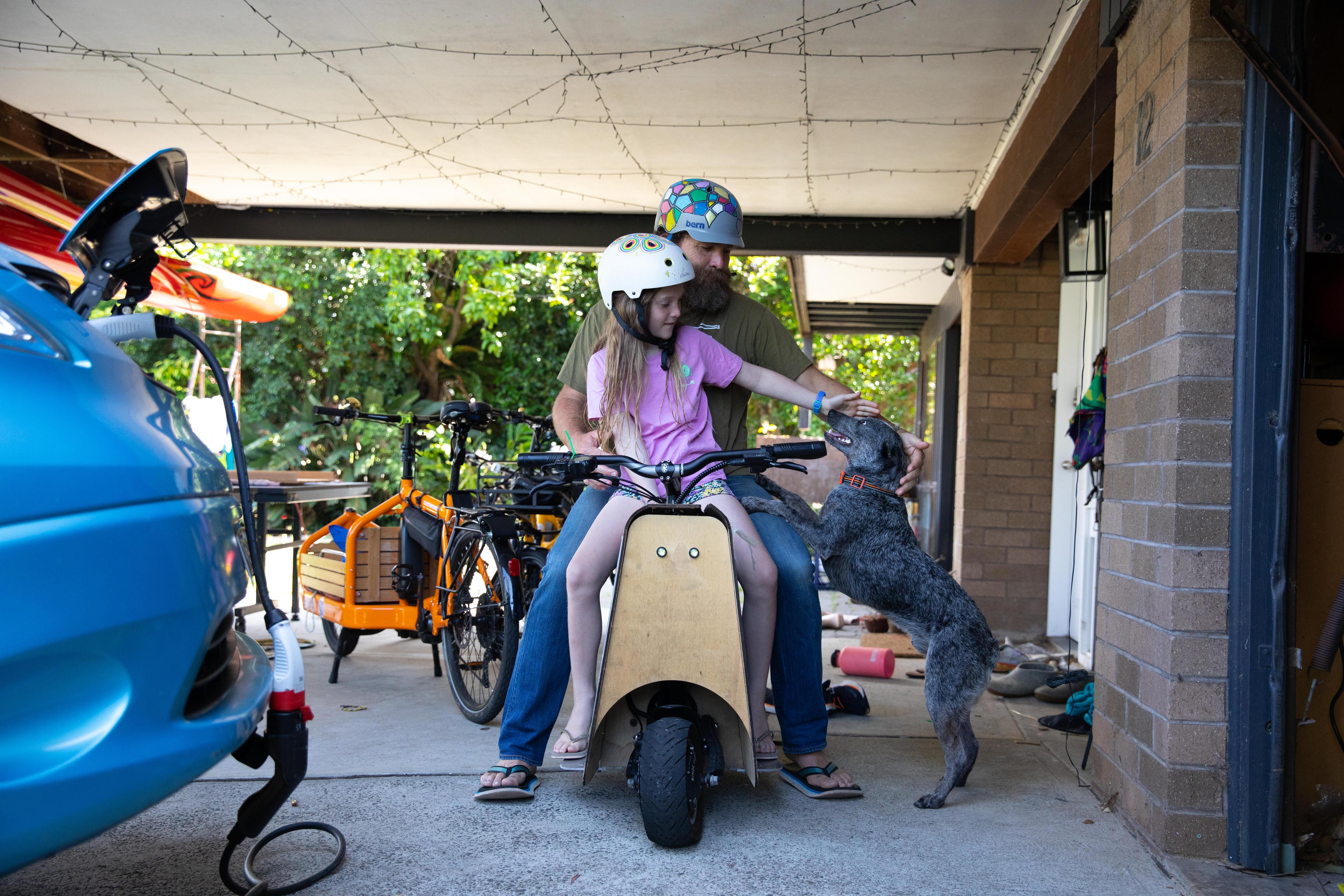 A man and a young girl wearing crash helmets sit on a scooter with wooden bodywork.
