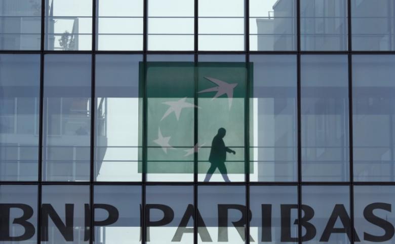 A man is seen in silhouette as he walks behind the logo of BNP Paribas in a building in Issy-les-Moulineaux, near Paris, France.