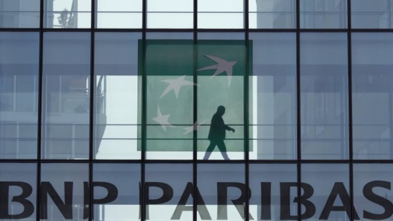 A man is seen in silhouette as he walks behind the logo of BNP Paribas in a building in Issy-les-Moulineaux, near Paris, France.