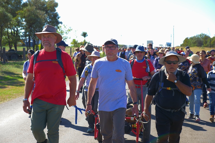 A large procession of pepole walk down a road.