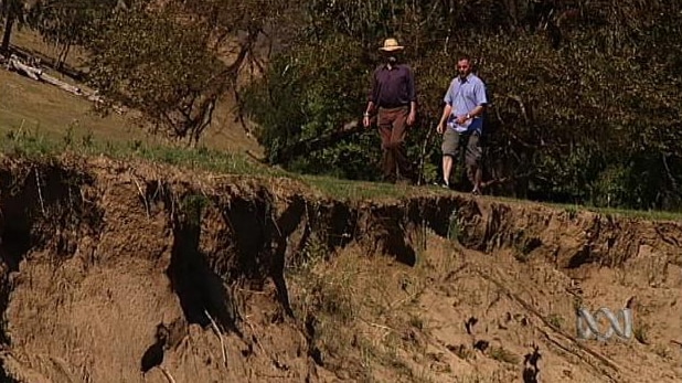 Two men walk alongside river edge with significant erosion