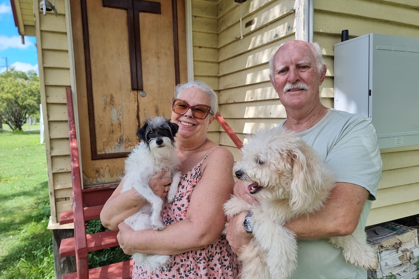 A woman wearing a pink dress and sunglasses holding a black and white dog, while her husband holds a fluffy white dog