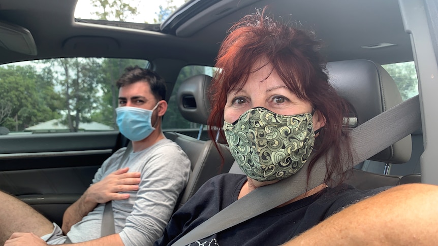 A woman and her teenage son sit in a car with masks on.