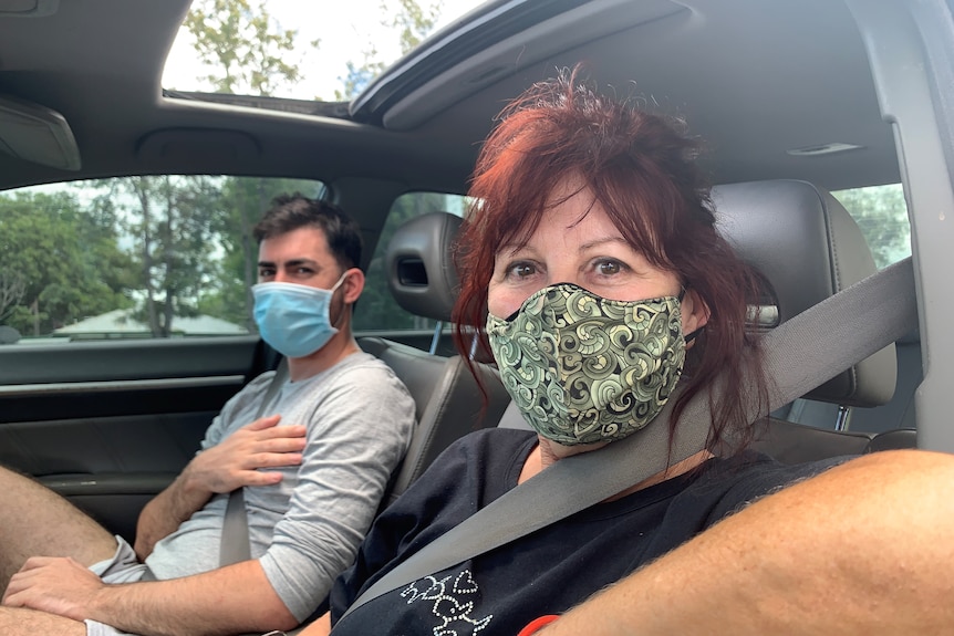 A woman and her teenage son sit in a car with masks on.