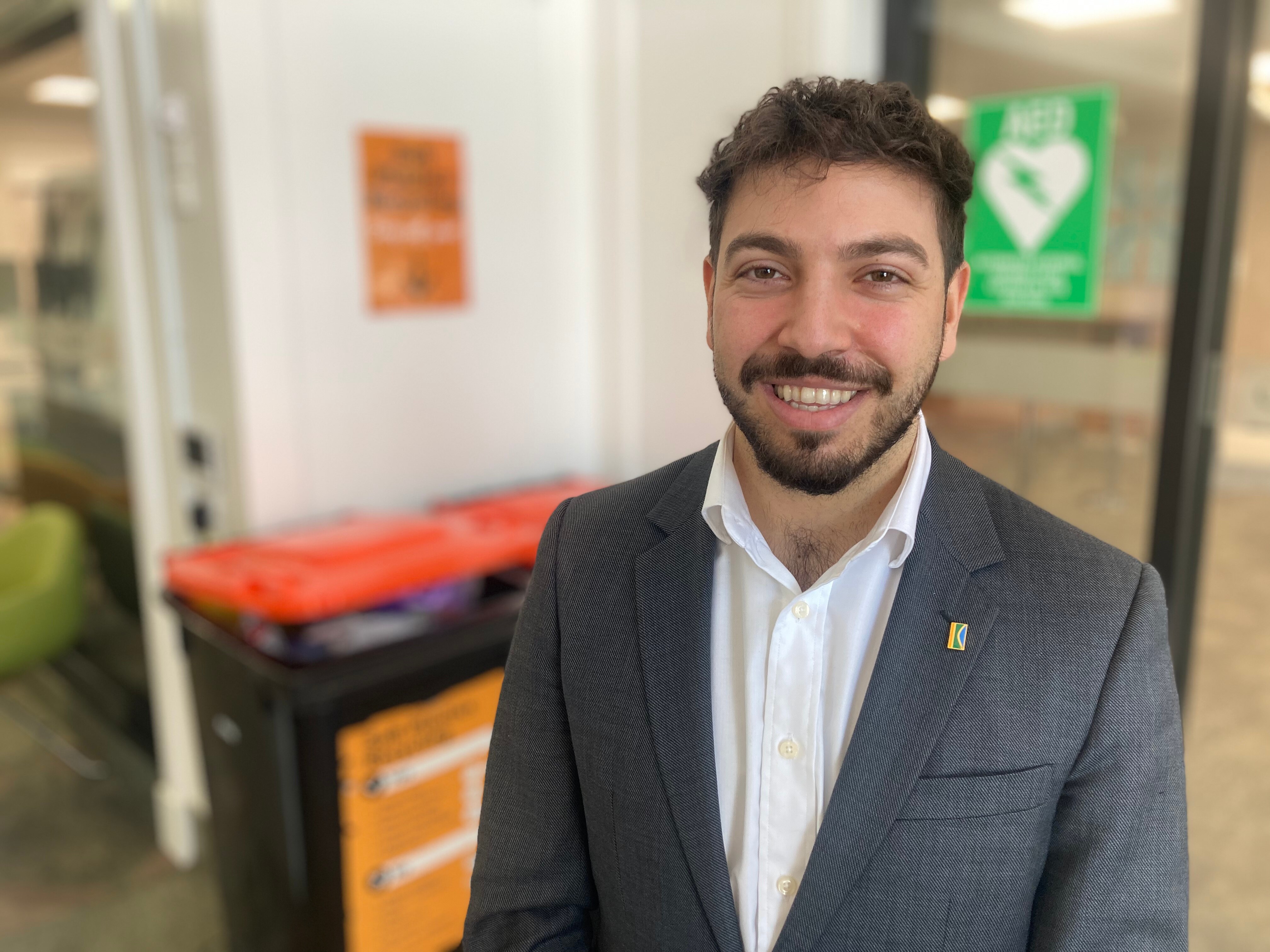 A man wearing a blazer and shirt stands in front of red-lidded bins.
