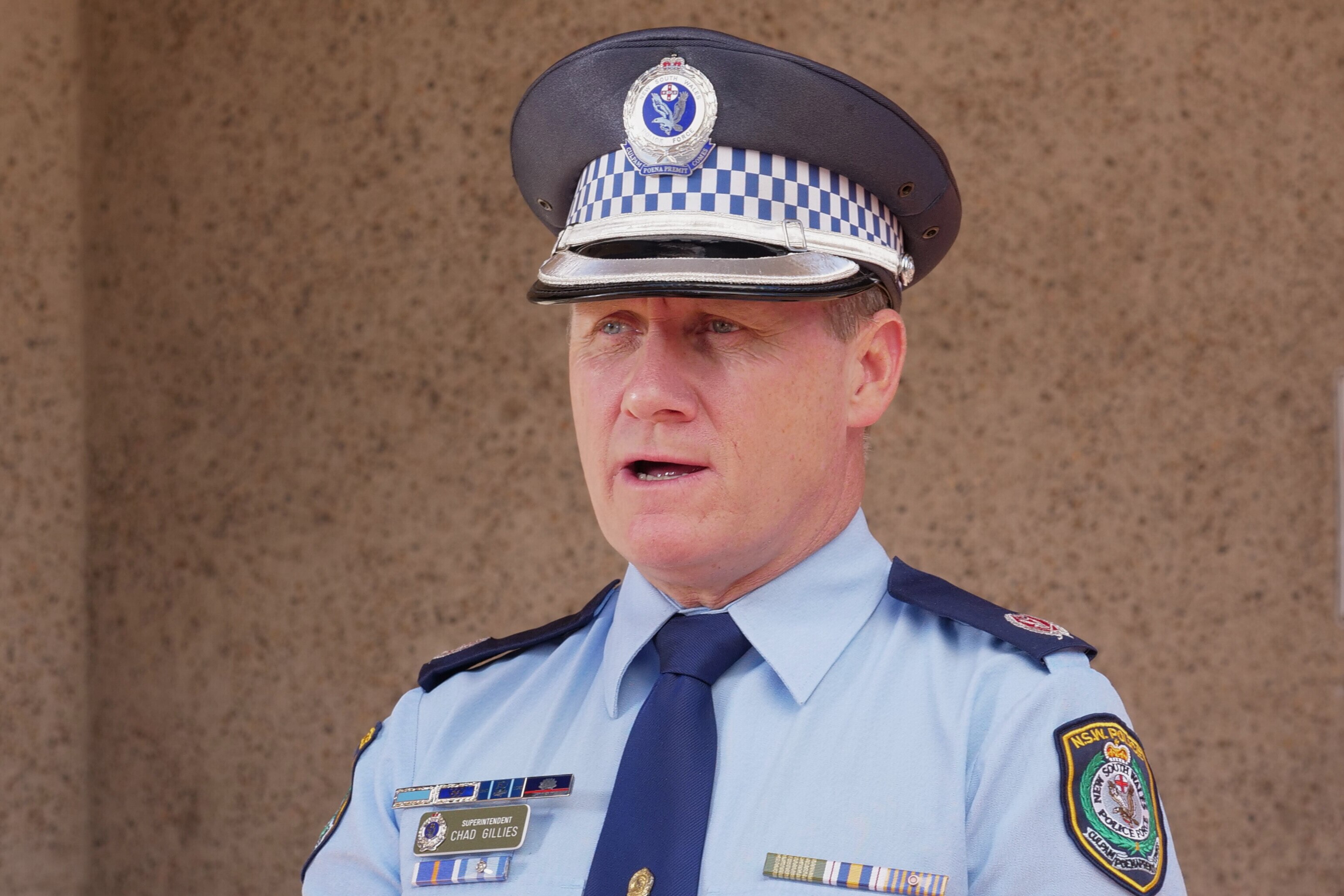A police officer wearing a police hat and blue uniform addressing the media. 